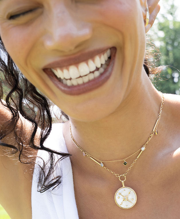 Woman wearing 18k gold gemstone necklace and mother of pearl constellation necklace